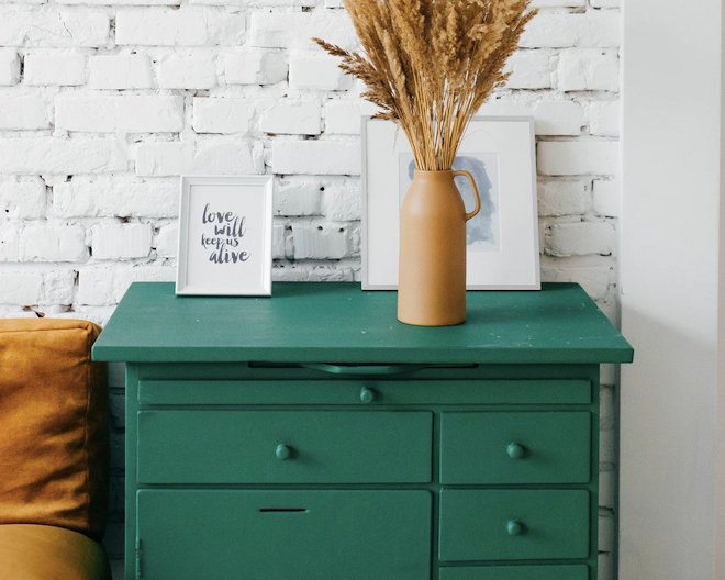 A green dresser with drawers and a vase of wheat